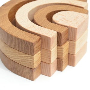 May include: A set of wooden rainbow arches, stacked in a half-circle shape. The arches are made of natural wood with a light brown and dark brown color variation.