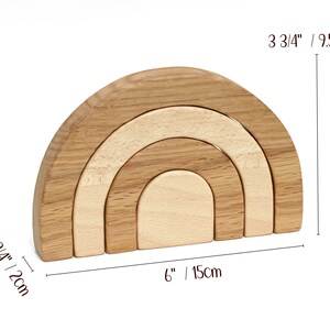 May include: Wooden rainbow stacking toy with four arches in different sizes. The largest arch is 3 3/4 inches tall and 6 inches wide. The toy is made of natural wood and has a light brown color.