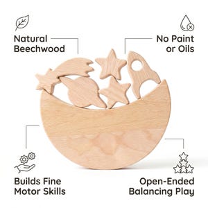 Pu&ograve; includere: Un set di blocchi impilabili in legno chiaro con una base a forma di mezzaluna e forme pi&ugrave; piccole tra cui un pianeta, stelle, un razzo e una stella cadente. Le etichette indicano Natural Beechwood, No Paint or Oils, Builds Fine Motor Skills e Open-Ended Balancing Play.