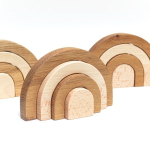 May include: Three wooden rainbow arches, each made of four interlocking pieces, with the largest arch at the back and the smallest arch in the front. The arches are made of natural wood with a light brown and cream color.