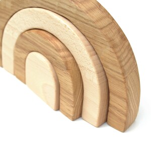 May include: A wooden rainbow stacking toy with three arches in different sizes. The arches are made of natural wood with a light brown color.