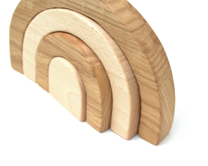 May include: A wooden rainbow stacking toy with three arches in different sizes. The arches are made of natural wood with a light brown color.