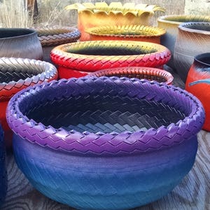 以下が含まれることがあります： リサイクルタイヤで作られたカラフルなプランターのコレクション。プランターは、パープル、ブルー、レッド、イエロー、ブラックなど、さまざまな色でペイントされています。プランターは、一番大きなプランターが前、一番小さなプランターが後ろになるように並べてあります。