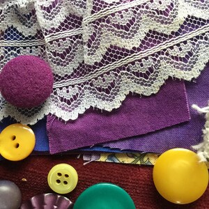 May include: A collection of purple and yellow buttons, some with four holes, and a purple fabric covered button. There is also white lace and purple fabric.