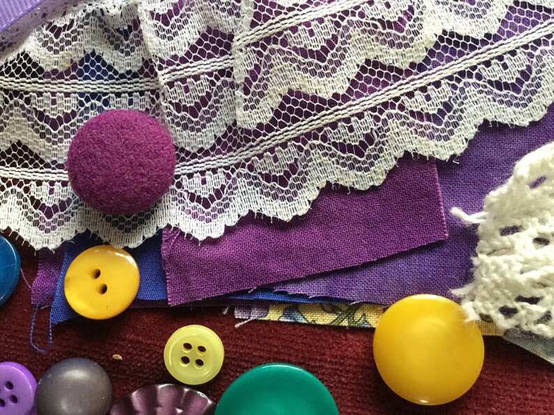 May include: A collection of purple and yellow buttons, some with four holes, and a purple fabric covered button. There is also white lace and purple fabric.