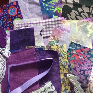 May include: A collection of purple and lavender fabric scraps, including floral prints, gingham, and solid colors. There is also white lace and a purple ribbon.