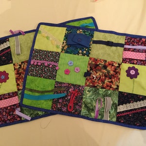 Puede incluir: Dos cuadrados de tela coloridos con varias texturas y adornos, incluyendo botones, cintas y encaje. Los cuadrados están cosidos juntos para crear una alfombra de juego sensorial táctil para bebés y niños pequeños.