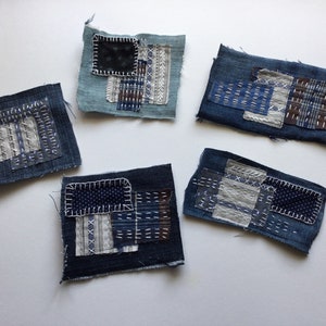 Op de afbeelding: Vijf kleine vierkanten van stof, elk gemaakt van verschillende tinten blauw denim en met een patchwork-ontwerp met verschillende stikpatronen.