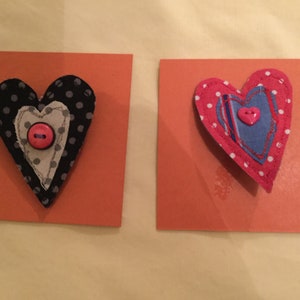 May include: Two handmade fabric hearts with pink polka dots and buttons. The hearts are layered and stitched together with different fabrics.