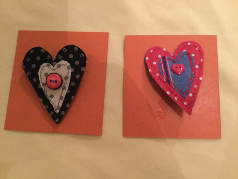May include: Two handmade fabric hearts with pink polka dots and buttons. The hearts are layered and stitched together with different fabrics.