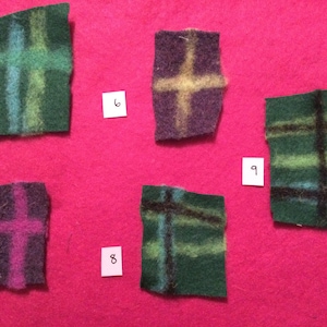 Puede incluir: Cinco cuadrados de fieltro con diseños de cruces en varios colores, incluyendo verde, azul, morado y negro, se muestran sobre un fondo rosa. Cada cuadrado tiene una combinación de colores única, creando un efecto de patchwork. Los números 5 al 9 están en pequeñas tarjetas blancas.