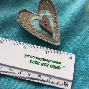 May include: A brown and white fabric heart with a smaller blue and white fabric heart inside. The hearts are sewn together and have a brown button in the center.