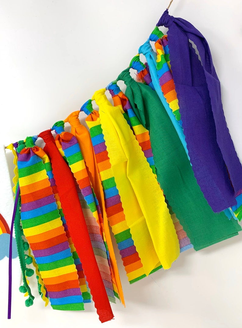 May include: A colorful rainbow-themed garland with fabric strips in various colors, including red, orange, yellow, green, blue, and purple. The garland is suspended from a string and is suitable for party decorations or festive occasions.