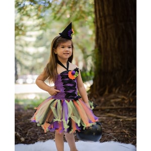 K&ouml;nnte beinhalten: Ein Halloween-Hexenkost&uuml;m f&uuml;r Kinder. Das Kleid ist lila, schwarz, orange und gr&uuml;n mit passendem Hut. Das Kind h&auml;lt einen schwarzen Kessel. Das Kost&uuml;m ist perfekt f&uuml;r das Trick-or-Treating.