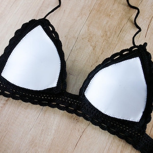 Puede incluir: Top de bikini negro de crochet con forro blanco. La parte superior tiene una forma triangular y está hecha de encaje de crochet delicado.