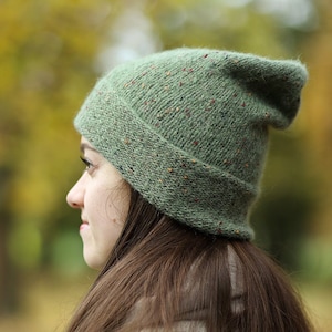May include: A green beanie with flecks of color throughout. The beanie is knit and has a slouchy fit.