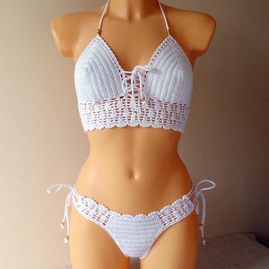 May include: White crochet bikini top and bottom with gold beads. The top has a halter style and ties in the front. The bottom has a low rise and ties on the sides.