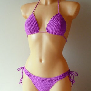 May include: A vibrant purple two-piece bikini set crafted with a detailed crochet knit pattern. The top features triangular cups with a scalloped edge and thin halter ties, while the matching bottom includes adjustable side ties for a secure fit.