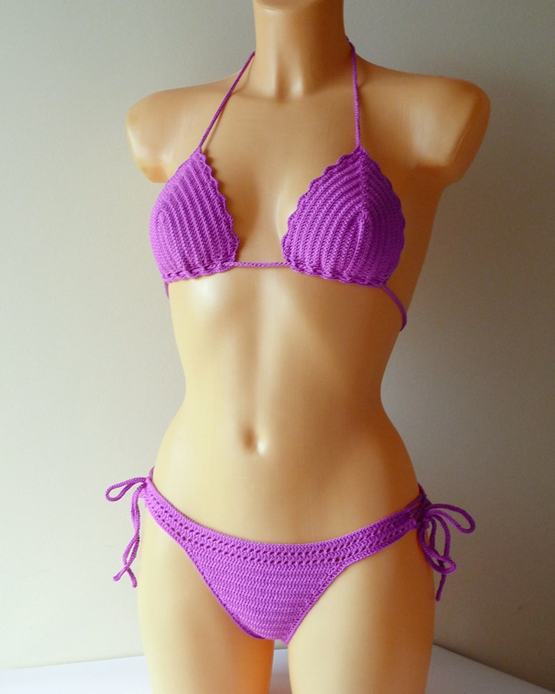 May include: A vibrant purple two-piece bikini set crafted with a detailed crochet knit pattern. The top features triangular cups with a scalloped edge and thin halter ties, while the matching bottom includes adjustable side ties for a secure fit.