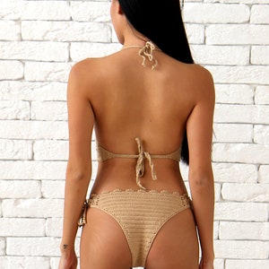 May include: A beige crochet bikini with a halter top and a high-cut bottom. The bikini is tied at the neck and back, and the bottom has a scalloped edge.