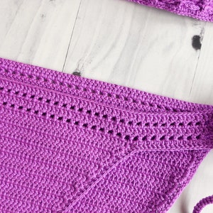 May include: A vibrant purple crochet bikini bottom featuring a dense, textured stitch pattern and a decorative horizontal band with openwork detailing along the upper edge, complemented by matching crochet ties at the side for a secure fit.