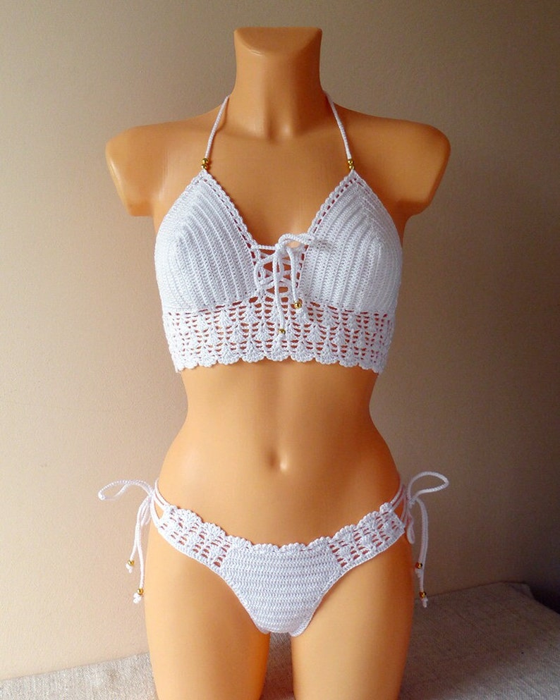 May include: White crochet bikini top and bottom with gold beads. The top has a halter style and ties in the front. The bottom has a low rise and ties on the sides.