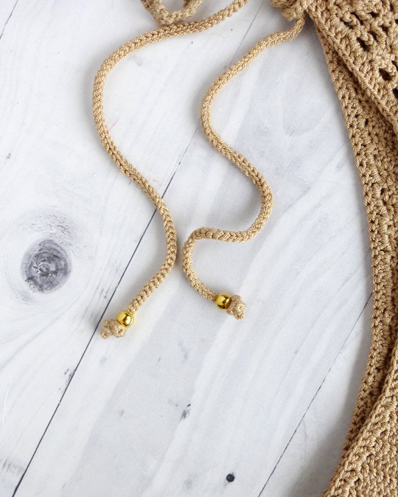 May include: Two beige cords with gold beads at the ends. The cords are on a white wooden surface.