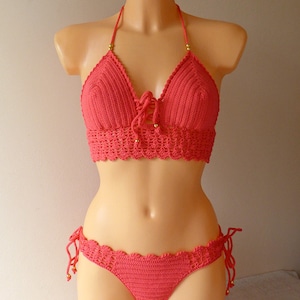 May include: A coral crochet bikini top and bottom with gold beads. The top has a halter style with a tie at the front. The bottom has a low rise and ties on the sides.