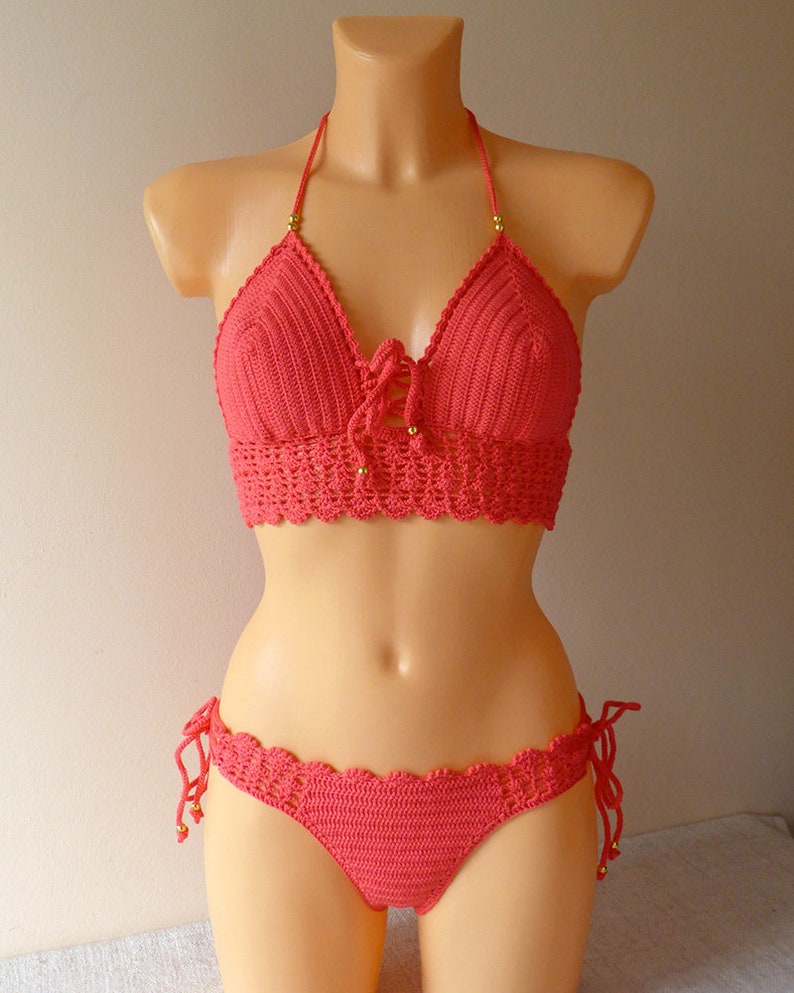 May include: A coral crochet bikini top and bottom with gold beads. The top has a halter style with a tie at the front. The bottom has a low rise and ties on the sides.