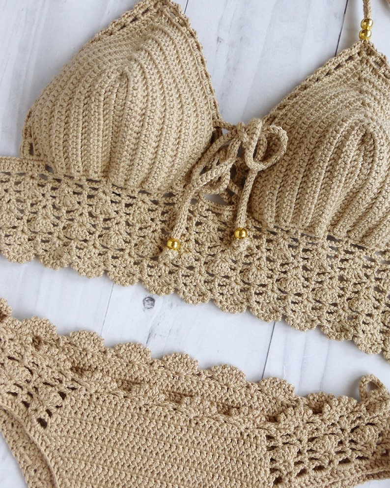 May include: A beige crochet bikini top and bottom with a scalloped edge. The top has a tie closure in the front and gold beads.