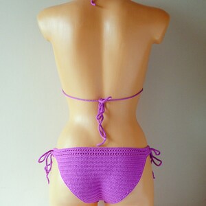 May include: A vibrant purple crochet bikini set featuring a halter-style top with adjustable tie closures at the neck and back, paired with matching bikini bottoms that include side tie details for a customizable fit and textured stitch pattern.