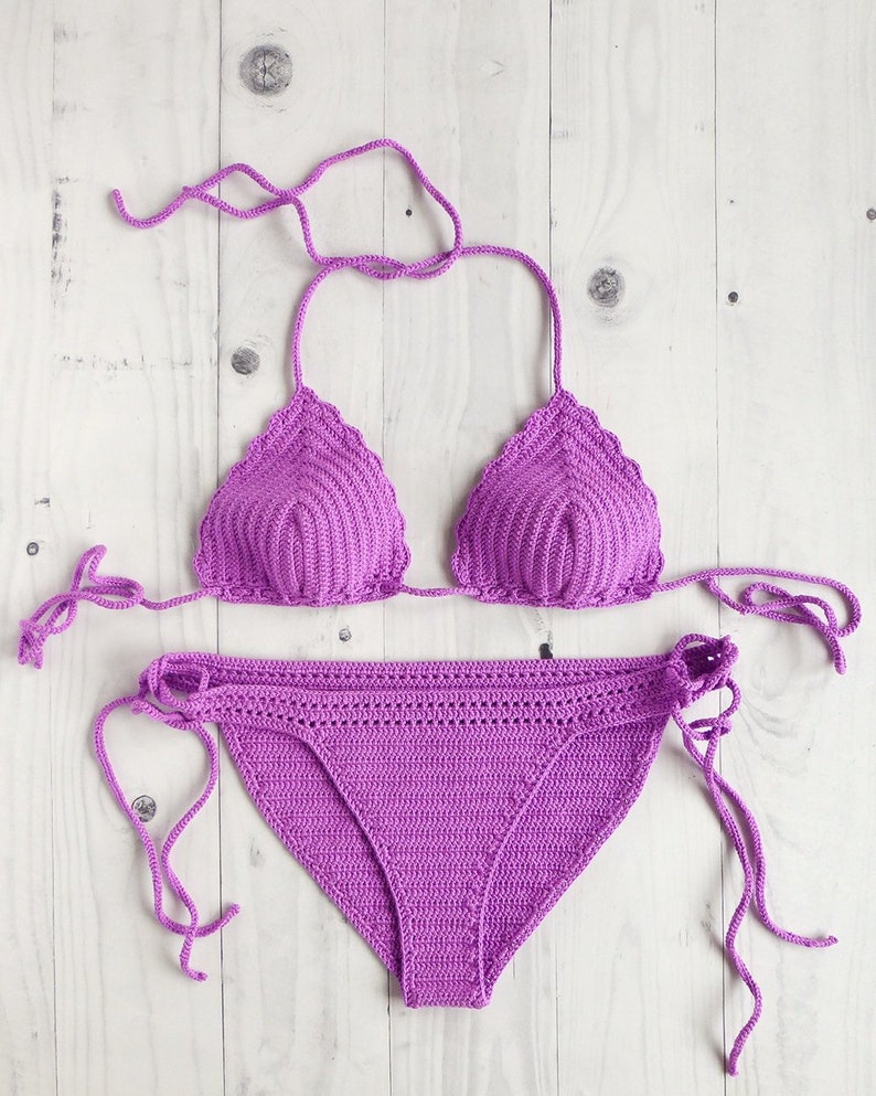 May include: A vibrant purple two-piece crochet bikini set. The top features triangular cups with scalloped edges and thin tie-strings. The matching bottom has adjustable side ties and a textured, hand-stitched pattern throughout the fabric.