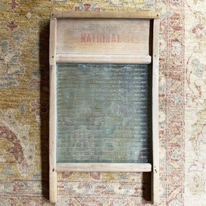 May include: A vintage wooden washboard with a glass insert. The washboard has a red inscription that reads "NATIONAL".