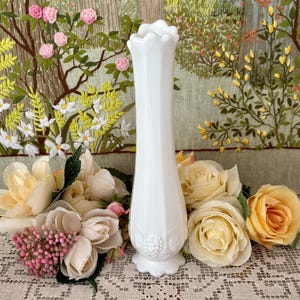 Peut inclure: Un vase blanc de style vintage avec un dessus festonn&eacute; et une base d&eacute;taill&eacute;e. Le vase est entour&eacute; de roses cr&egrave;me et p&ecirc;che et de fleurs roses. L'arri&egrave;re-plan pr&eacute;sente une tapisserie florale brod&eacute;e.
