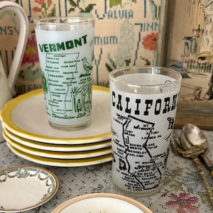 May include: Two vintage glass tumblers, one labeled "VERMONT" with a map and the other "CALIFORNIA" with a map. The glasses are on a yellow-rimmed plate. Also, small decorative plates with floral designs and a white pitcher with a floral design.