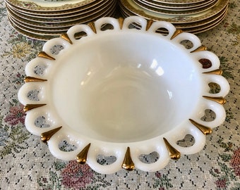 May include: A white milk glass bowl with a gold rim and scalloped edge. The bowl is empty and sitting on a floral tablecloth.