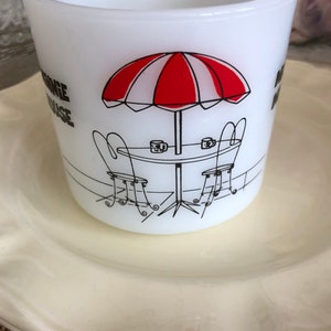 May include: White ceramic mug with a black and red illustration of a table with two chairs and an umbrella. The text "Orange House" is printed on the mug.