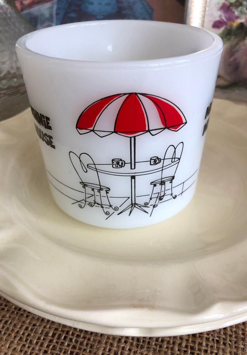 May include: White ceramic mug with a black and red illustration of a table with two chairs and an umbrella. The text "Orange House" is printed on the mug.