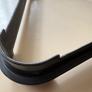 K&ouml;nnte beinhalten: Ein schwarzer, dreieckiger Ausstecher mit abgerundeter Ecke und gezackten Kanten. Der Ausstecher ist aus Metall und liegt auf einer hellen Oberfl&auml;che.