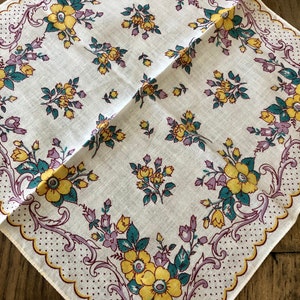 K&ouml;nnte beinhalten: Quadratisches wei&szlig;es Taschentuch mit floralem Muster. Das Design zeigt gelbe und lila Blumen mit gr&uuml;nen Bl&auml;ttern, umrahmt von einem gewellten Rand mit einem gepunkteten Muster. Das Taschentuch ist diagonal gefaltet.