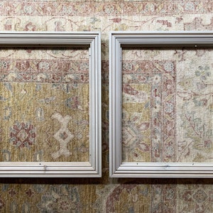 May include: Two white wooden picture frames, each with a simple, rectangular design. The frames are placed side-by-side against a patterned rug.