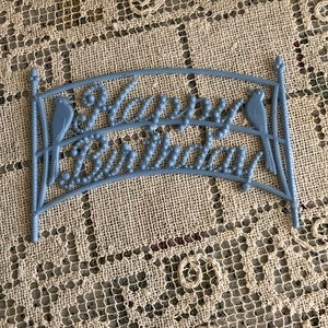 May include: Blue plastic cake topper with the words "Happy Birthday" and two birds on either side.