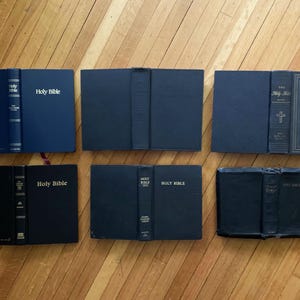 May include: A collection of seven black hardback books with gold lettering. The books are all titled "Holy Bible".