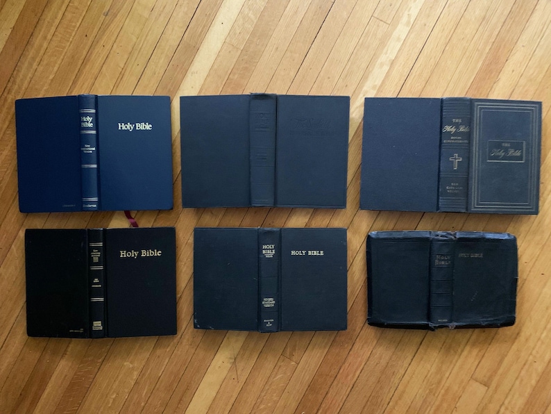 May include: A collection of seven black hardback books with gold lettering. The books are all titled "Holy Bible".