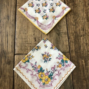 K&ouml;nnte beinhalten: Zwei Vintage-Taschent&uuml;cher mit Blumenmustern. Eines zeigt gelbe Rosen und ein lila Schleifendesign auf wei&szlig;em Hintergrund mit gelbem Rand. Das andere hat gelbe und lila Blumen mit einem gewellten Rand.