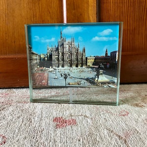 May include: A glass picture frame with a photo of the Duomo di Milano, a large cathedral in Milan, Italy. The photo shows the front facade of the cathedral and the square in front of it.