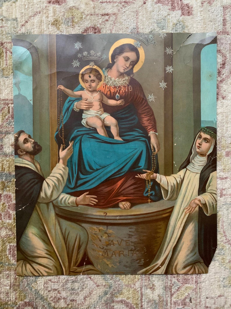 May include: A vintage religious print depicting the Virgin Mary holding a baby Jesus. The image features a blue and red robe, a crown of stars, and a rosary. Two figures, a man and a woman, are kneeling on either side of the Virgin Mary.