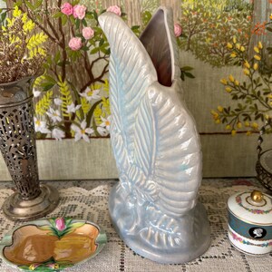 以下が含まれることがあります： 天使の羽の形をした水色のセラミック花瓶。 花瓶は質感のある表面と広い開口部を持っています。 その他のアイテムには、小さな灰皿、装飾的な金属の花瓶、小さな小物入れなどがあります。