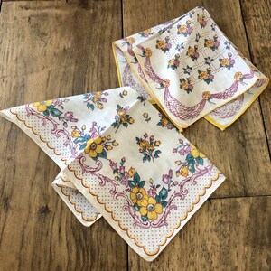 K&ouml;nnte beinhalten: Zwei Vintage-Taschent&uuml;cher mit Blumenmustern. Die Taschent&uuml;cher zeigen gelbe, lila und t&uuml;rkisfarbene Blumen auf wei&szlig;em Hintergrund. Eines hat einen gewellten Rand mit Punkten, das andere eine dekorative Bord&uuml;re.