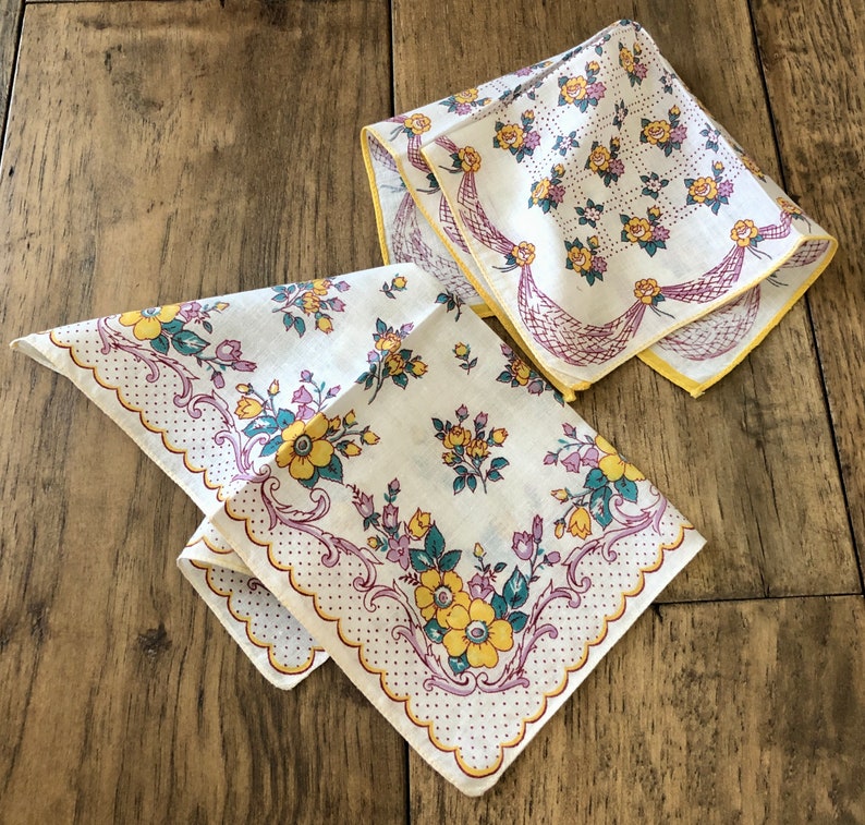 K&ouml;nnte beinhalten: Zwei Vintage-Taschent&uuml;cher mit Blumenmustern. Die Taschent&uuml;cher zeigen gelbe, lila und t&uuml;rkisfarbene Blumen auf wei&szlig;em Hintergrund. Eines hat einen gewellten Rand mit Punkten, das andere eine dekorative Bord&uuml;re.